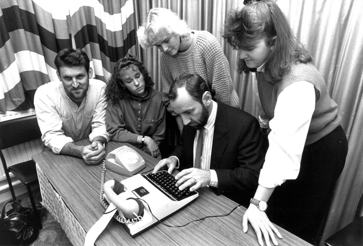 Staff gather around to look at a TTY device. It resembles a typewriter with a phone receiver on the top. Victorian Deaf Society established Australia’s first TTY relay service (circa 1980).