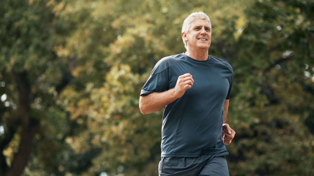 A fit older man goes running in a park.