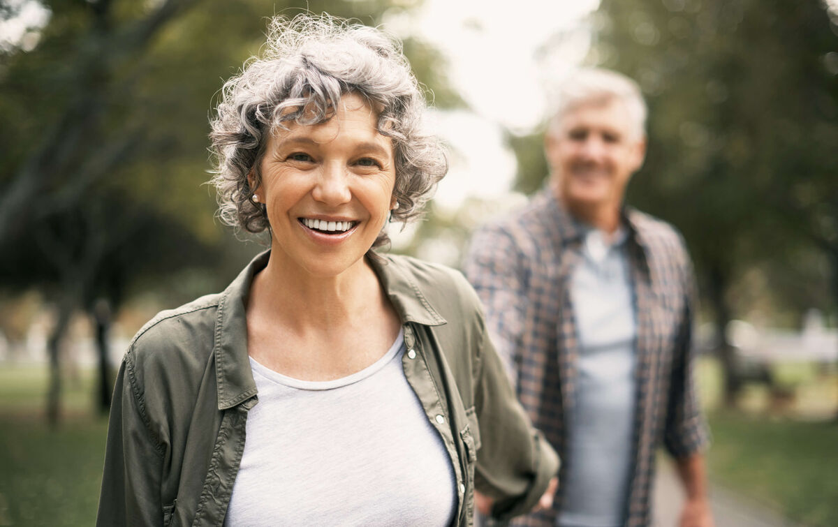 A smiling middle-aged couple are walking hand-in-hand in the park.