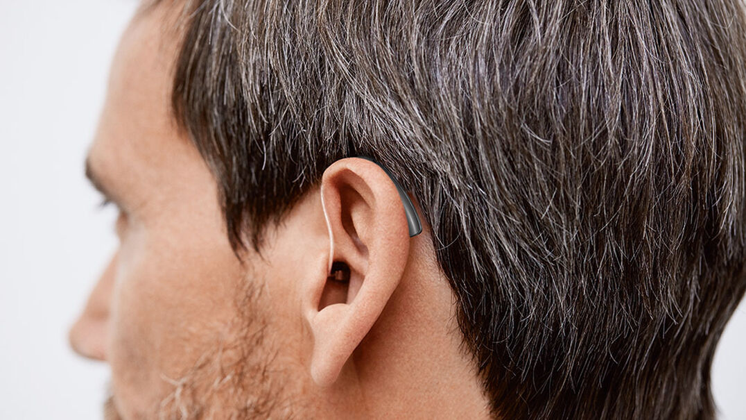 A close up of a man's head. You can see he is wearing a small behind-the-ear hearing aid. Expression Audiology can help you find the hearing aid that best suits your lifestyle.