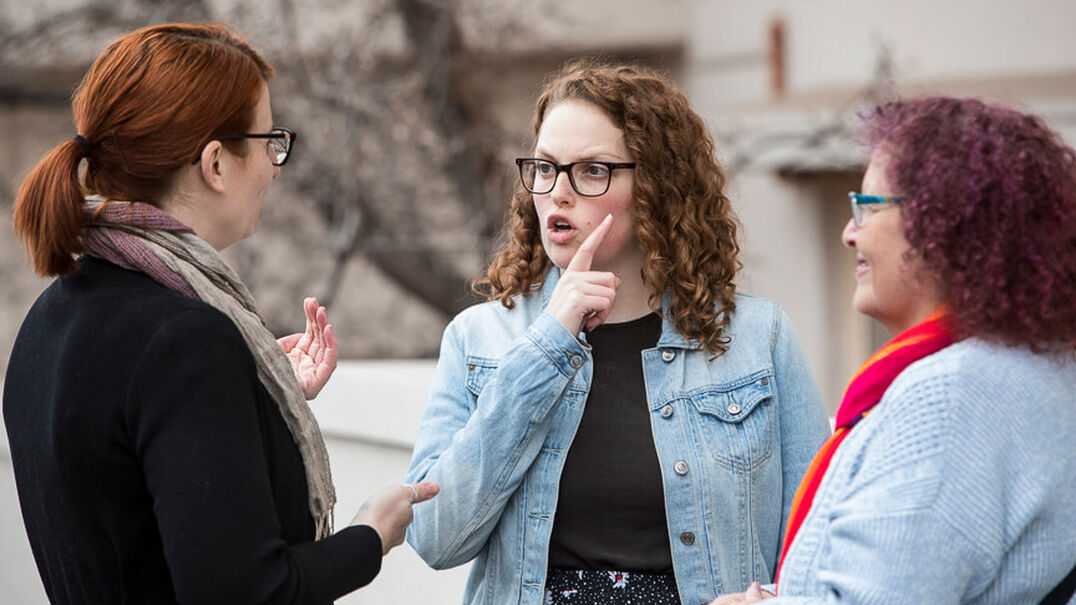 Three woman of varying ages are having a friendly conversations using Auslan. They are outside in front of a building. Learn Auslan with Expression Australia.